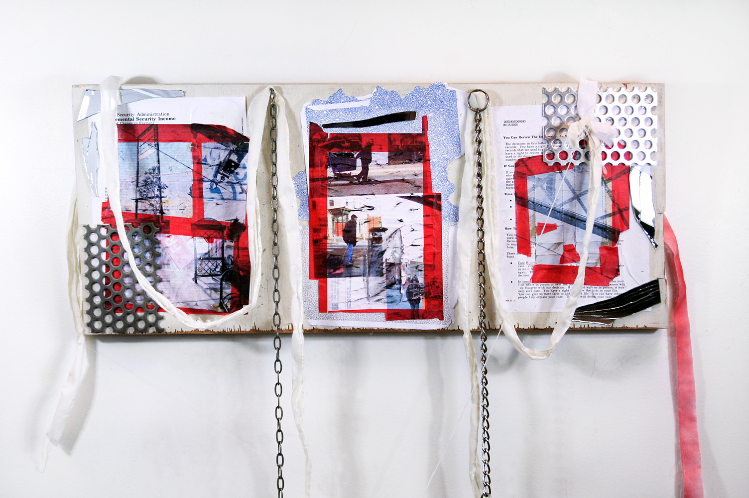 Three rectangular collages are mounted across a sawn fragment of a white‑painted hollow‑core door. Each collage layers red tape, photo transfers, envelopes, metal grating, and mirror shards over typewritten paperwork. Torn fabric strips and lengths of metal chain hang from the top edge, extending below the panel. The door’s plywood fibers are visible where paint has settled and chipped. In the left collage, red tape frames a government form beneath floating photographic fragments and pierced metal. The center collage overlays patterned envelopes with taped rectangles and street photographs partially obscured by black marks. The right collage combines red tape outlines, gridded imagery, metal mesh, and cracked mirror pieces. Reflective surfaces, repeated rectangles, and suspended materials emphasize fragmentation, weight, and structure.